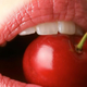 Close-up of woman's mouth biting into bright red cherry